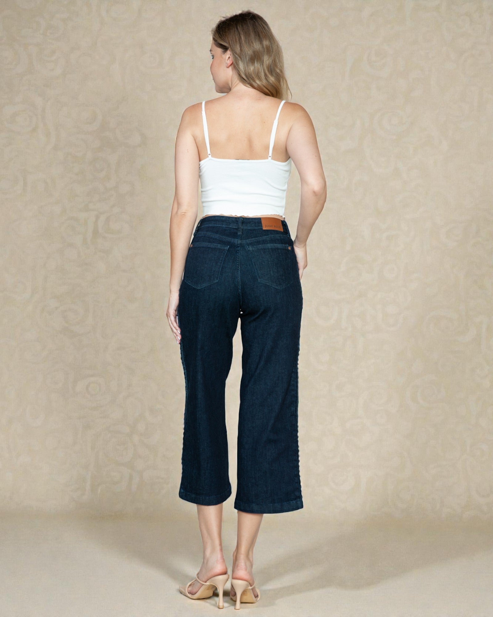 Woman wearing dark blue jeans and a white top against a beige background