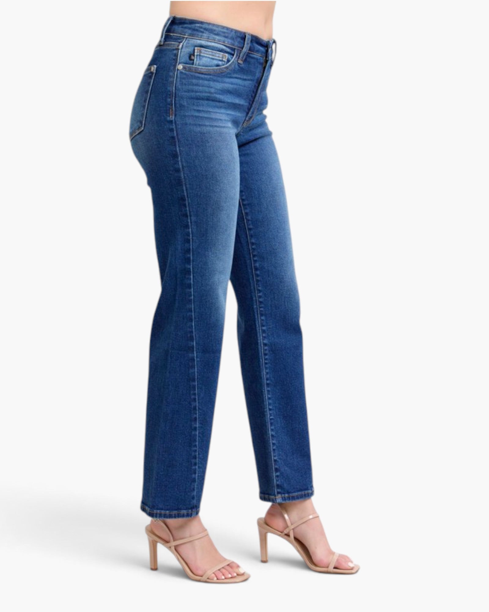 A model wearing a pair of medium wash blue denim jeans with a straight-to-regular leg fit, paired with beige heeled sandals, shown from a side profile against a light gray studio background.