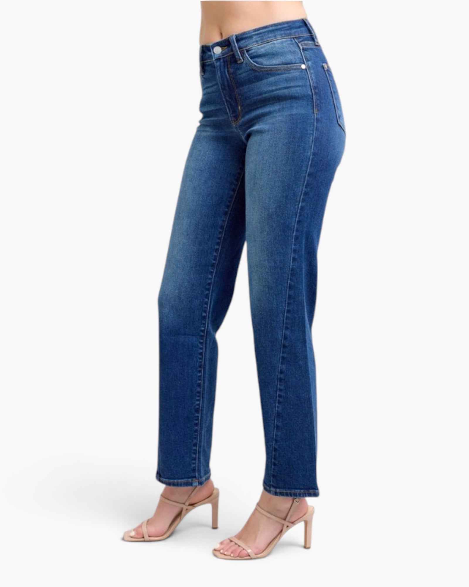 A model wearing a pair of medium wash blue denim jeans with a straight-leg fit, paired with beige strappy high-heeled sandals, shown from the waist down on a light gray background.