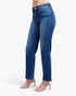A model wearing a pair of medium wash blue denim jeans with a straight-leg fit, paired with beige strappy high-heeled sandals, shown from the waist down on a light gray background.