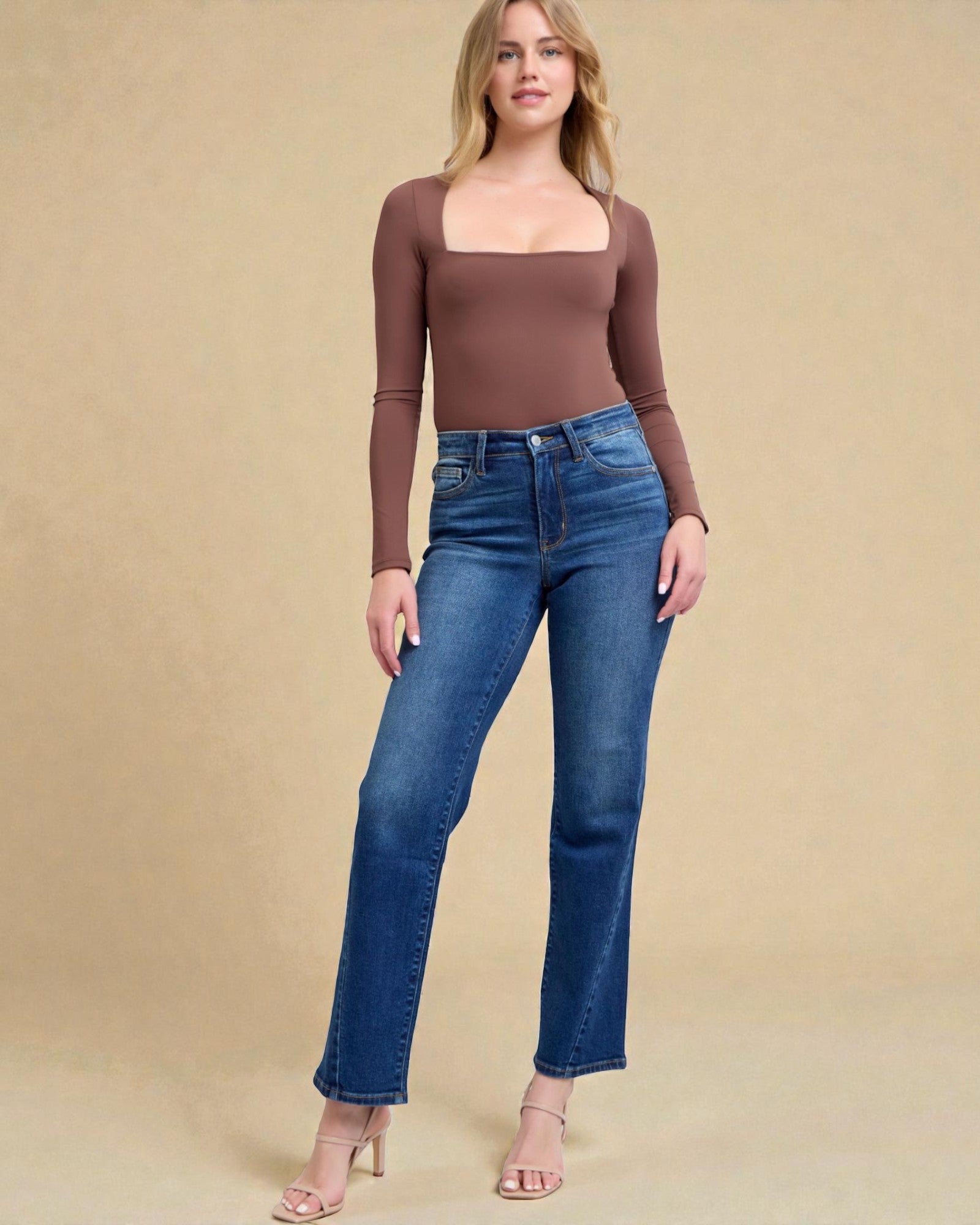 Woman wearing a brown long-sleeve top and blue jeans on a beige background