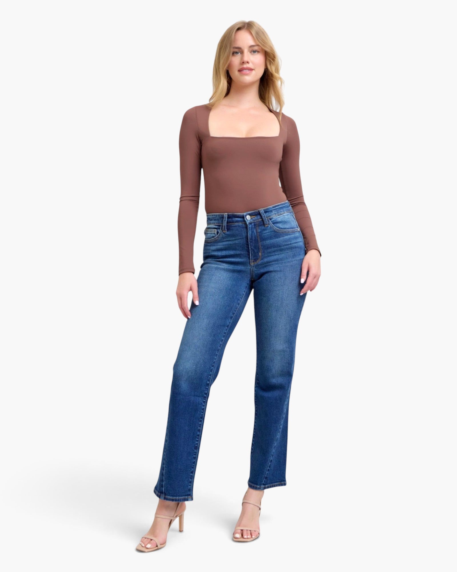 A woman modeling a brown long-sleeve square-neck top and blue straight-leg jeans against a light gray studio background.