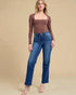 Woman wearing a brown long-sleeve top and blue jeans on a beige background