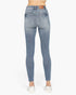 Rear view of a person wearing light blue skinny jeans with white slip-on shoes against a plain white background.