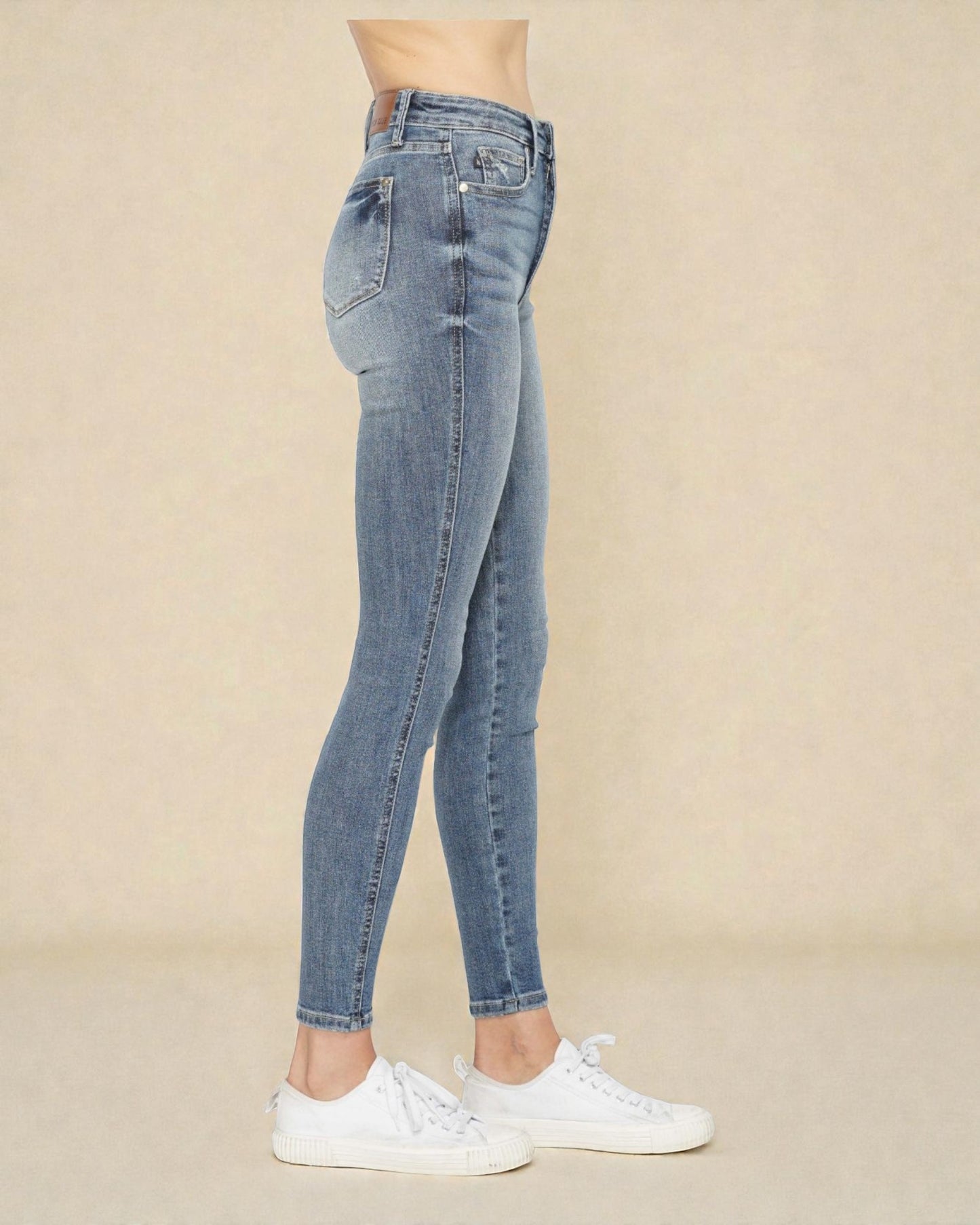 Person wearing light blue jeans and white sneakers on a beige background