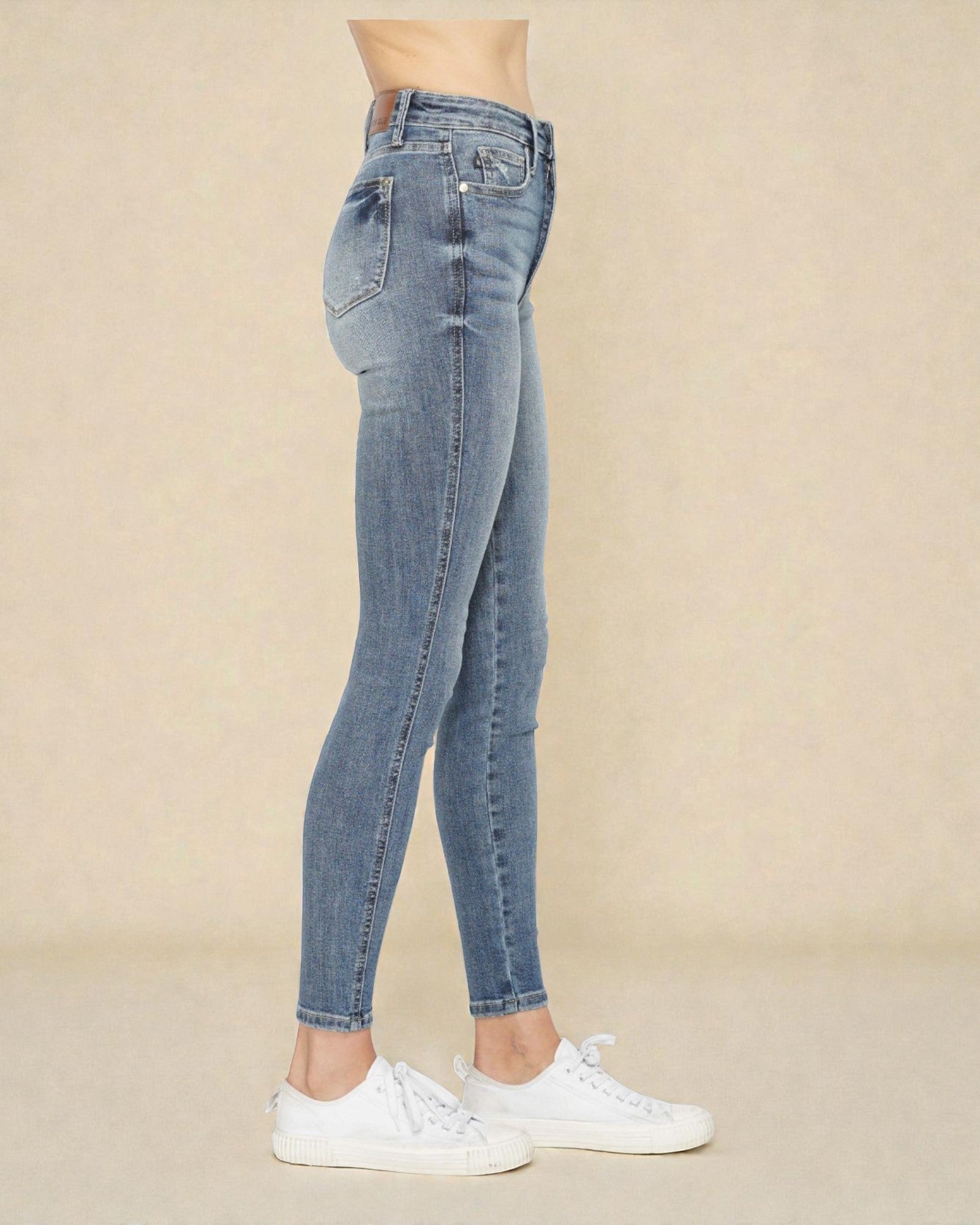 Person wearing light blue jeans and white sneakers on a beige background