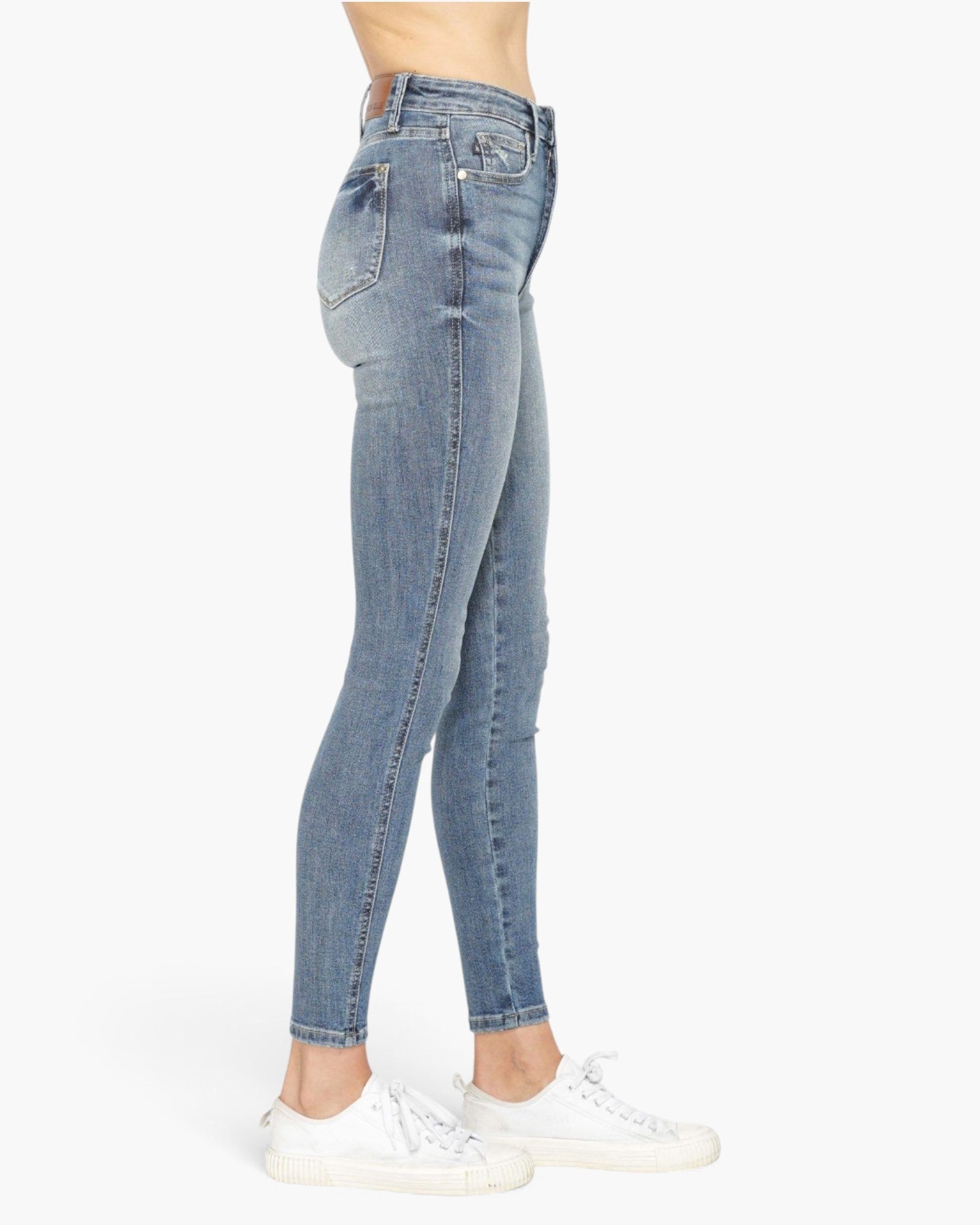A side profile view of a person wearing light-wash blue skinny jeans and white sneakers against a plain white background.