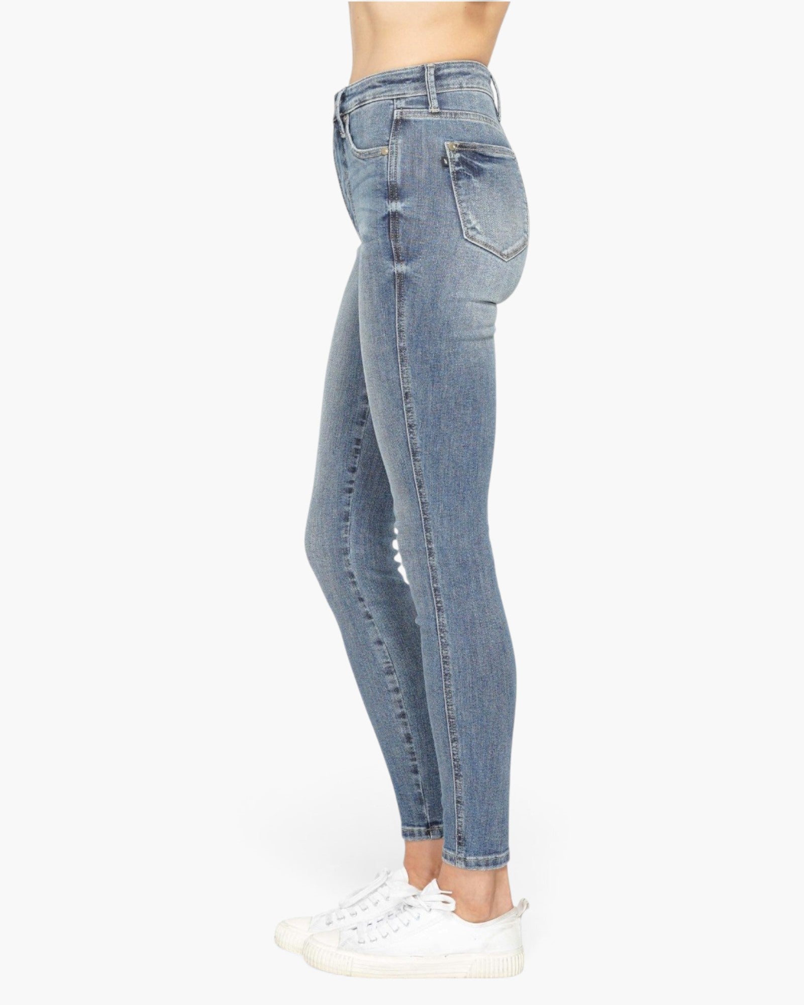 Side view of a person wearing light blue high-waisted skinny jeans with white sneakers, shown against a plain white studio background.