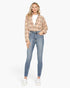 A woman modeling a beige and brown plaid flannel shirt over a white t-shirt, paired with blue skinny jeans and white sneakers, against a plain white background.