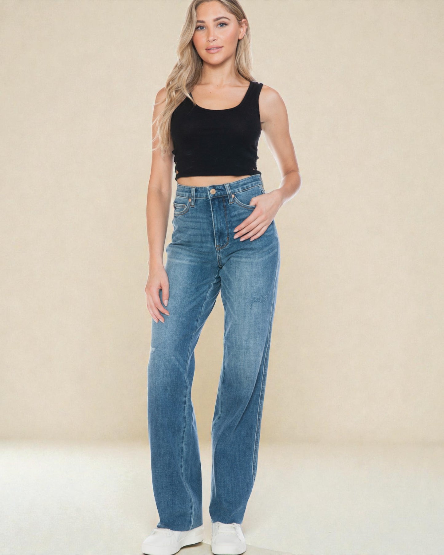 Woman wearing blue jeans and a black top against a beige background