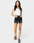 Woman wearing a white top and black denim shorts on a plain background