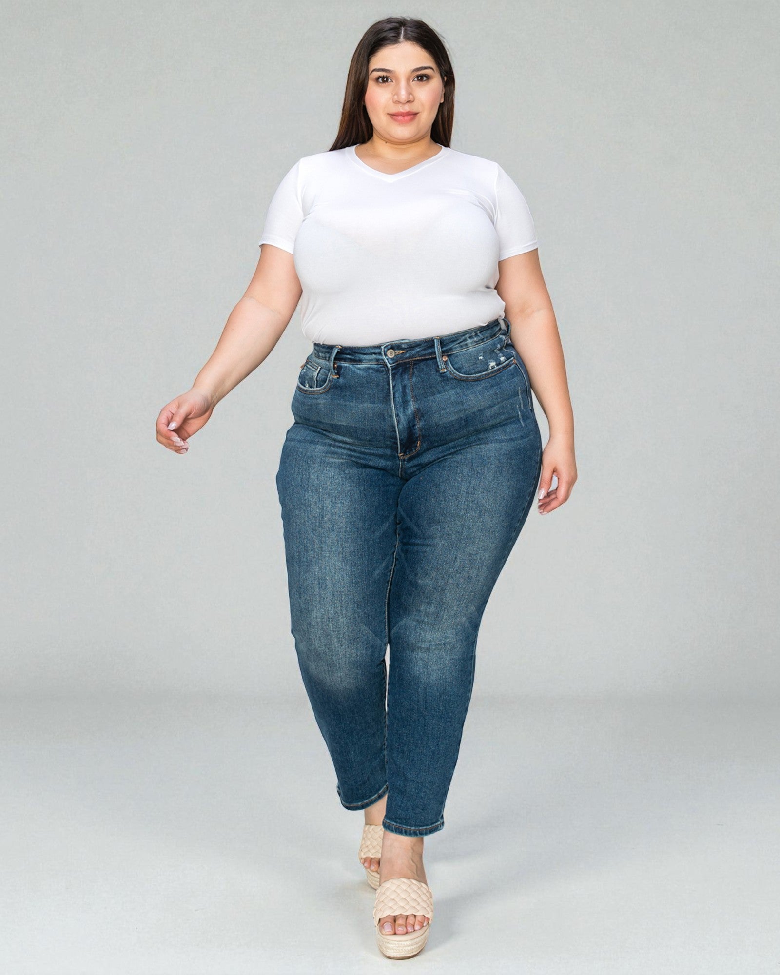 Woman wearing a white t-shirt and blue jeans on a gray background