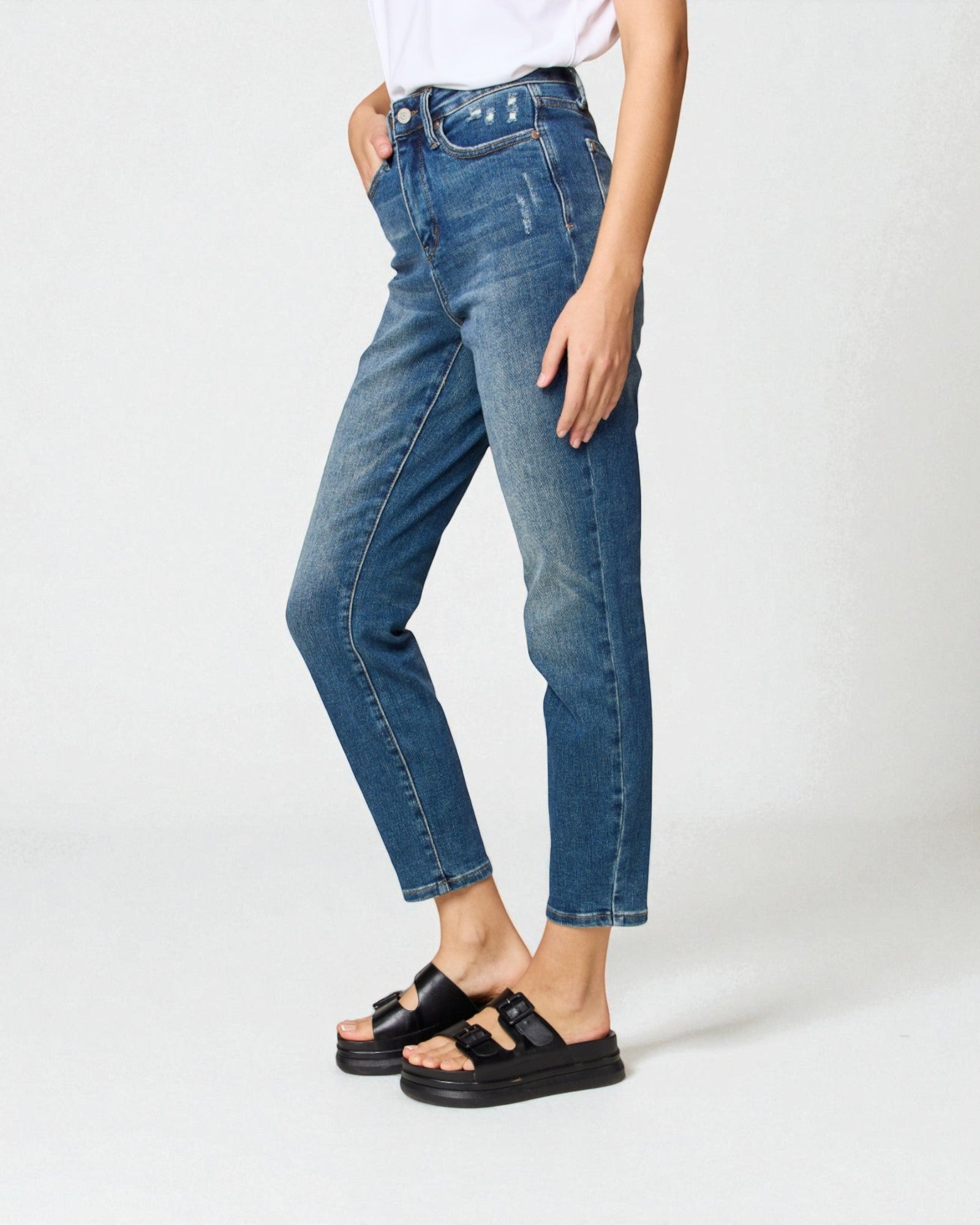 Person wearing blue jeans and black sandals on a white background