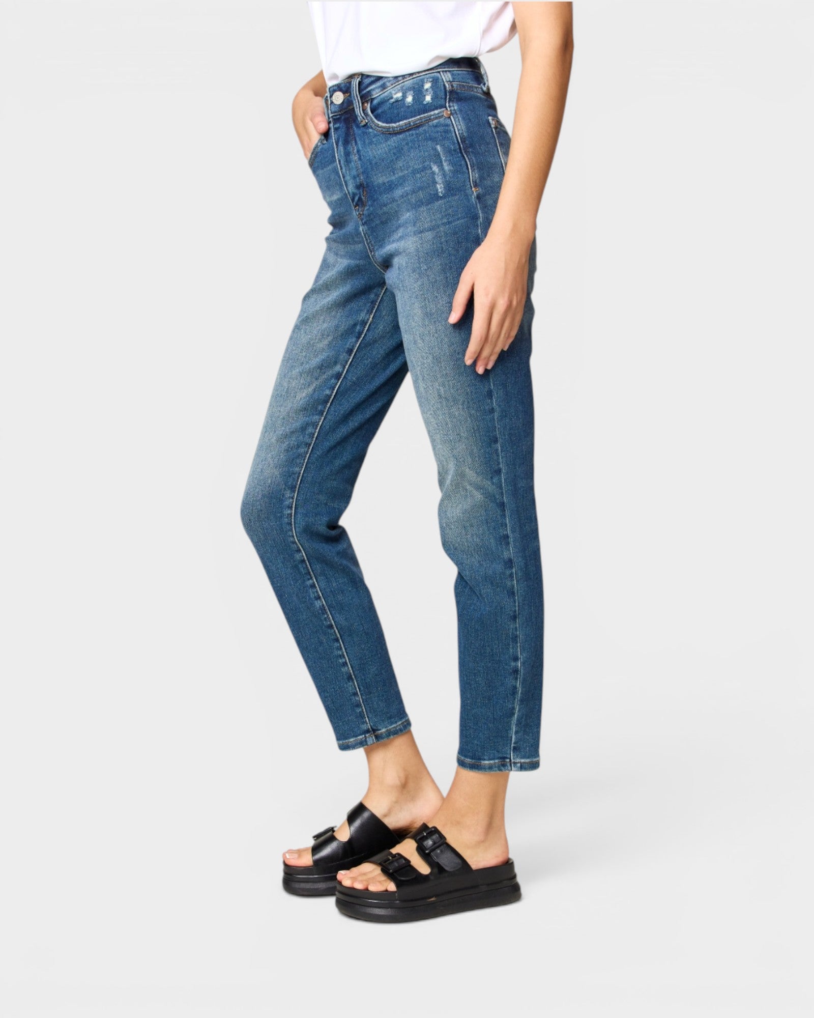 Person wearing blue jeans and black sandals on a white background
