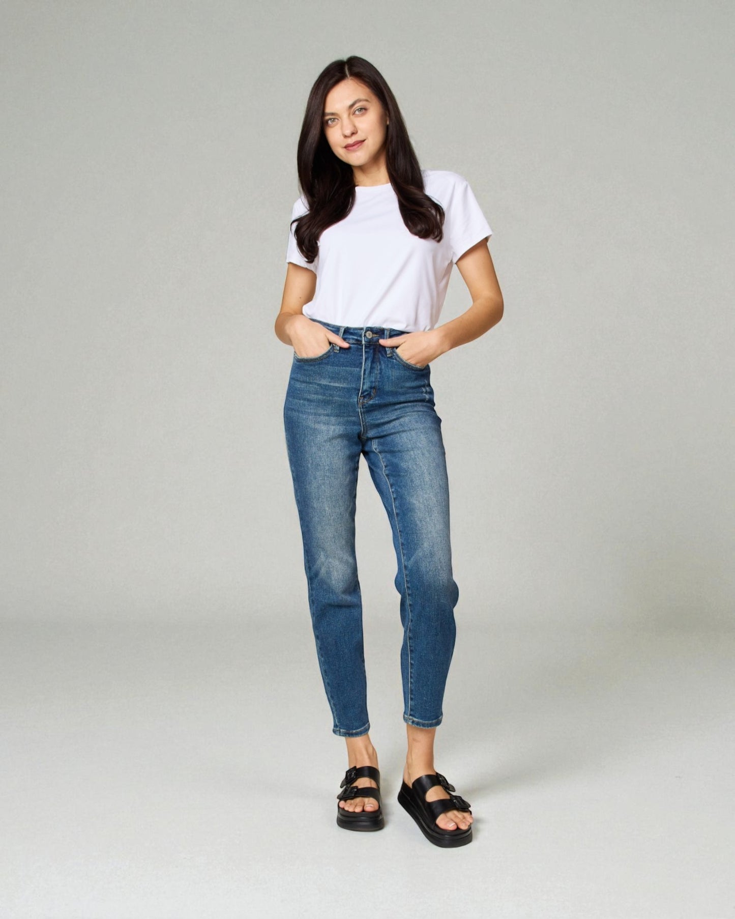Woman wearing a white t-shirt and blue jeans on a gray background