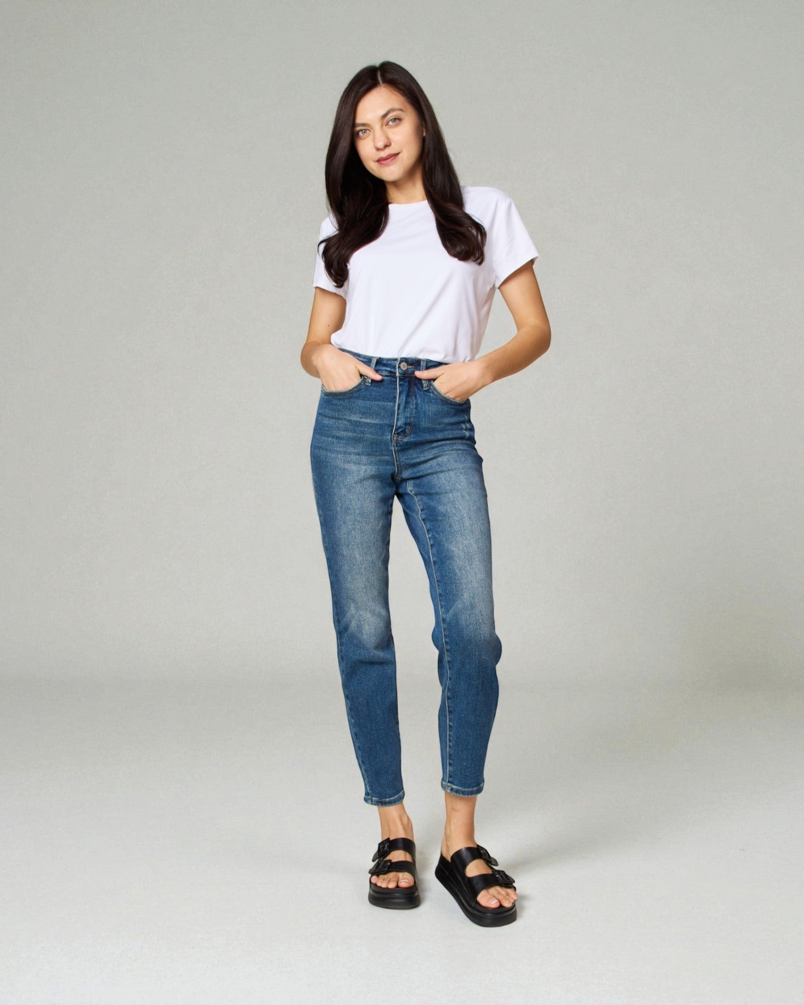 Woman wearing a white t-shirt and blue jeans on a gray background