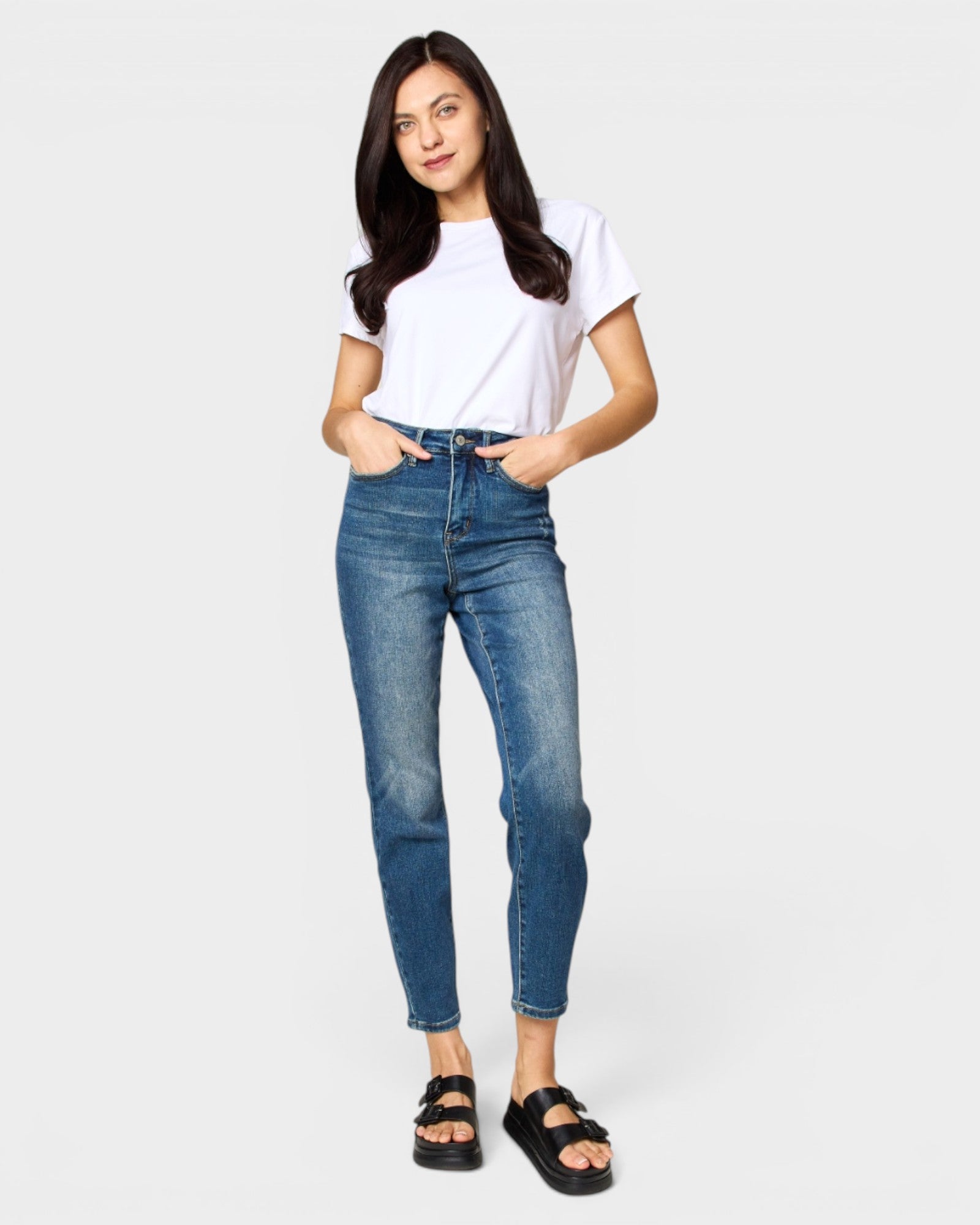 Woman wearing blue jeans and a white t-shirt on a plain background