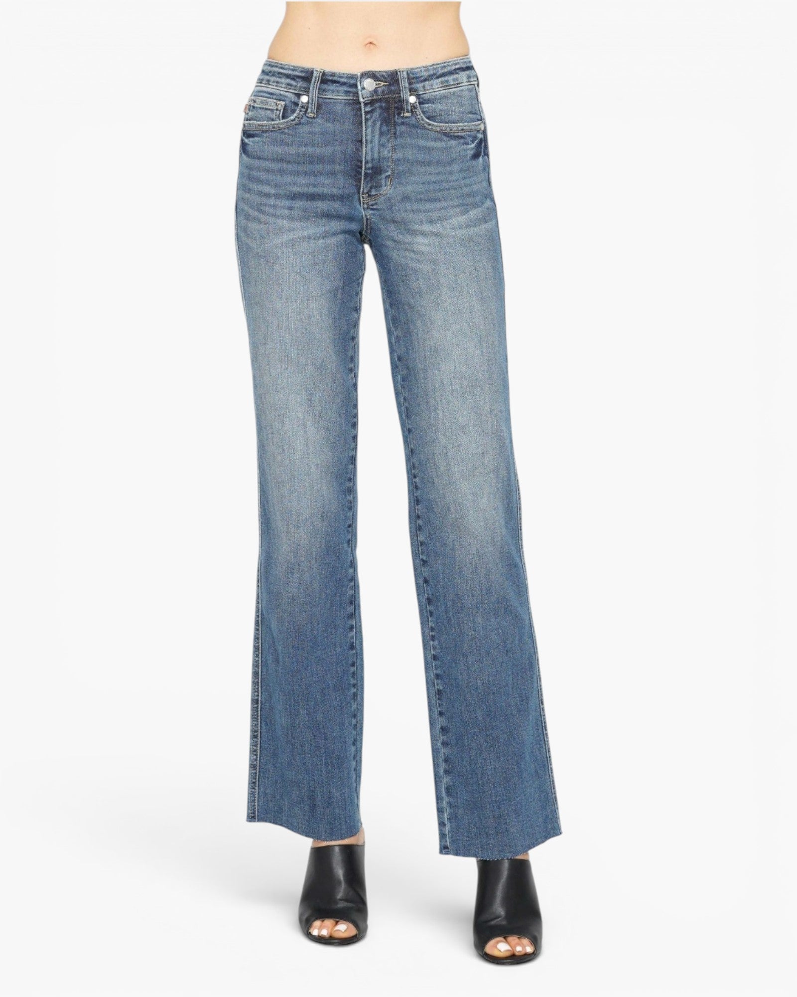 A person wearing medium-wash blue denim flare jeans with a straight-to-wide leg cut, paired with black open-toe heeled sandals, shown against a plain white studio background.