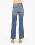 Rear view of a person wearing blue denim jeans with a straight-to-medium leg fit, paired with black and tan block-heel sandals, against a plain white studio background.