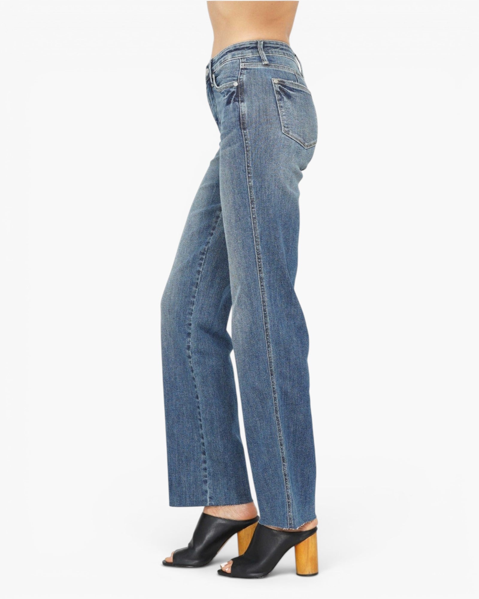 A side profile view of a person wearing medium-wash blue denim jeans with black peep-toe mule heels against a plain white background.
