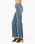 A side profile view of a person wearing medium-wash blue denim jeans with black peep-toe mule heels against a plain white background.