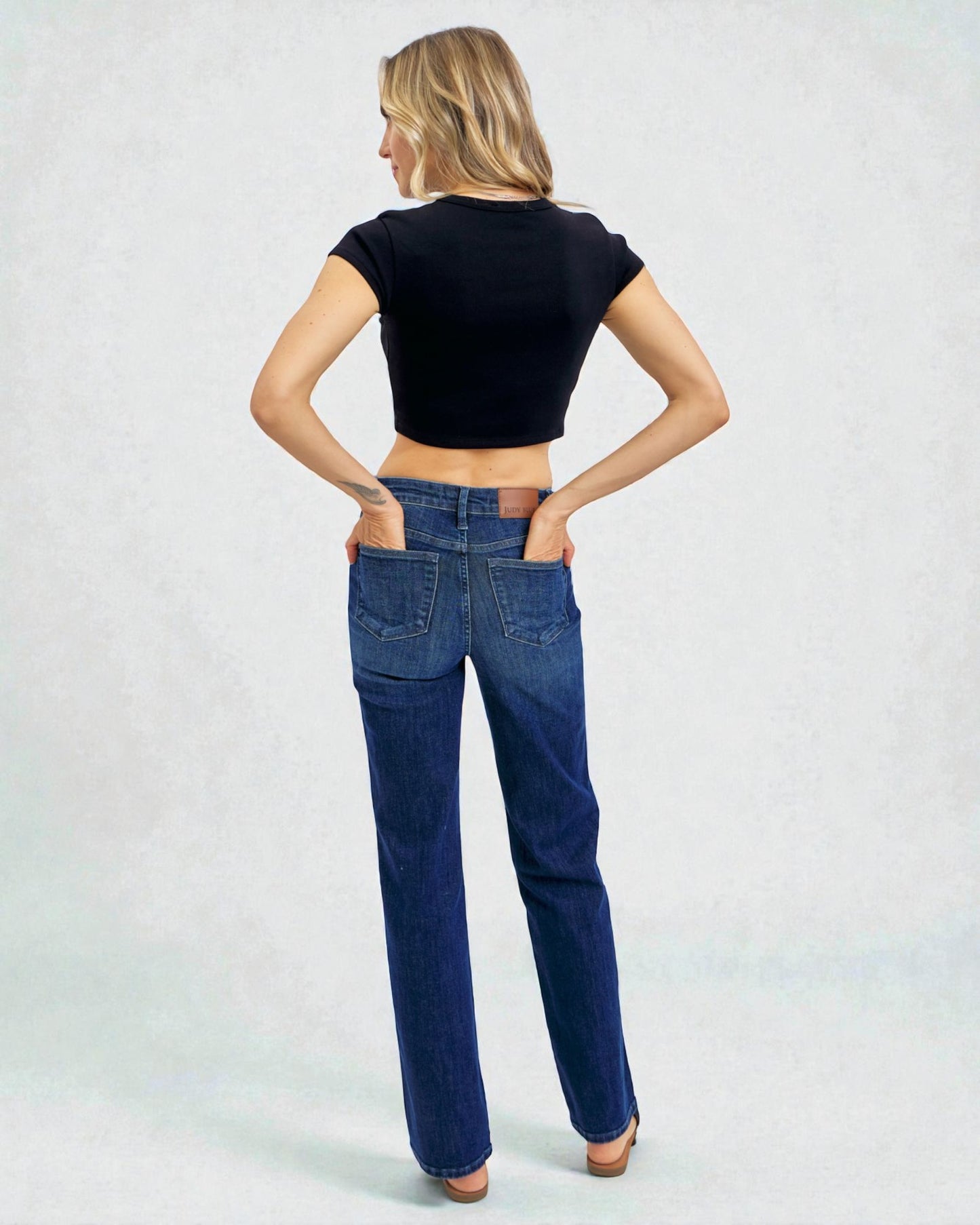 Woman wearing blue jeans and a black crop top on a light gray background