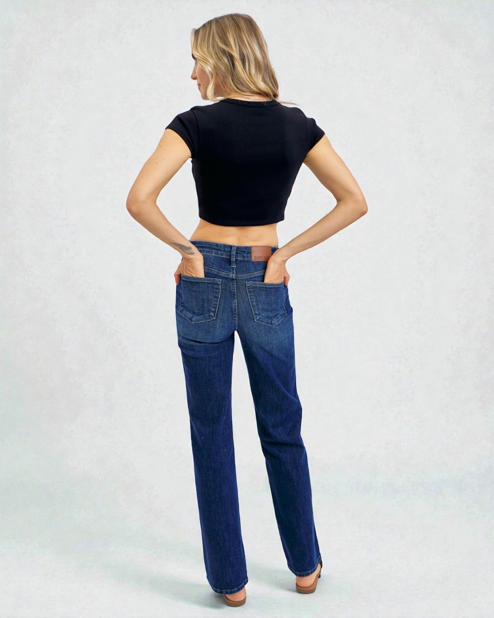 Woman wearing blue jeans and a black crop top on a light gray background