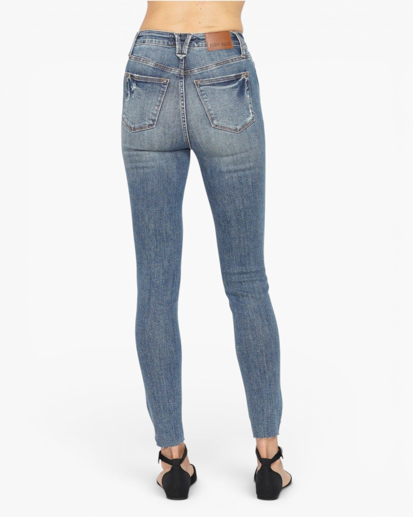 Rear view of a model wearing blue skinny jeans with black wedge sandals against a plain white background.