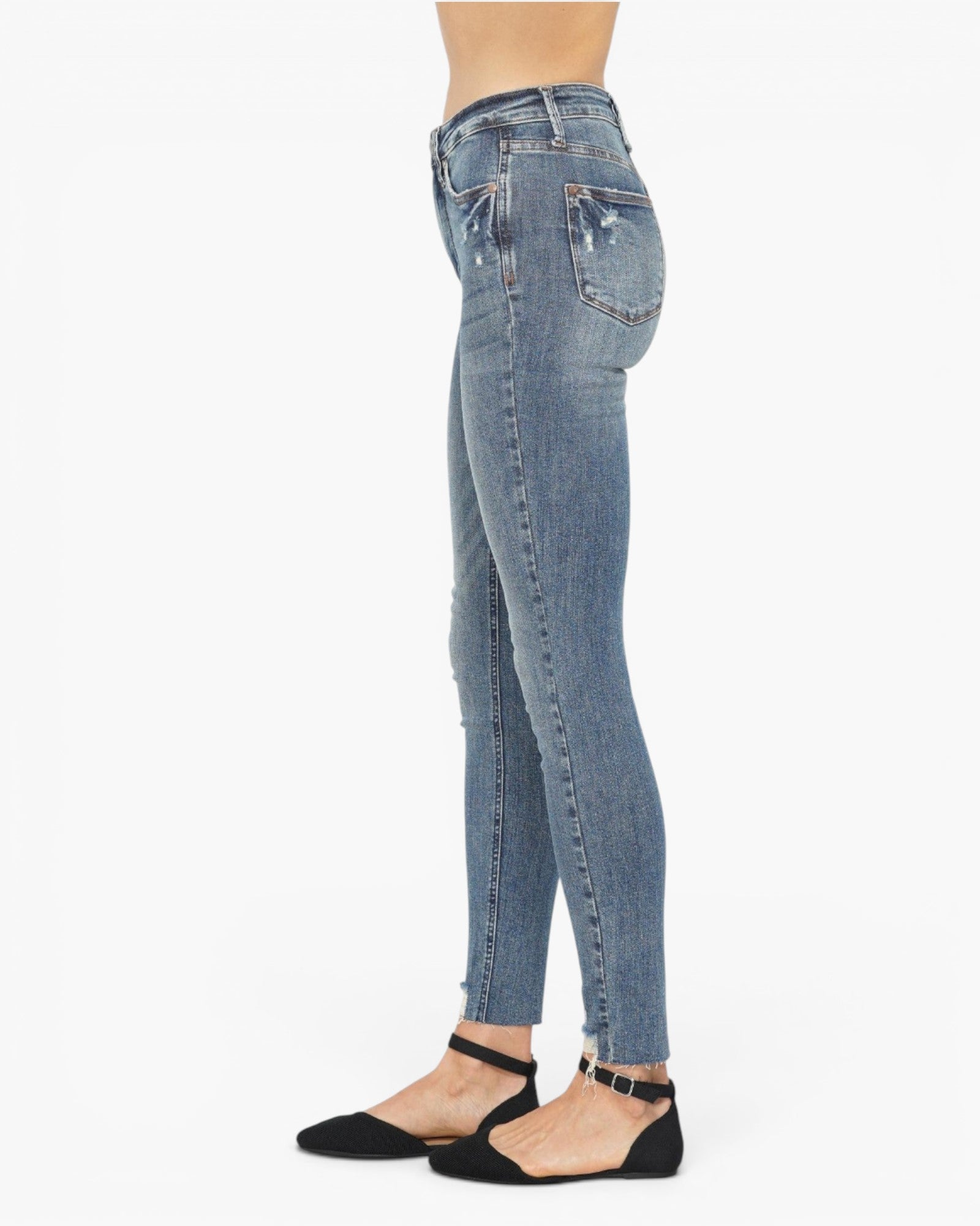 A side profile view of a model wearing light blue high-waisted skinny jeans with distressed details, paired with black flat sandals, against a plain white background.