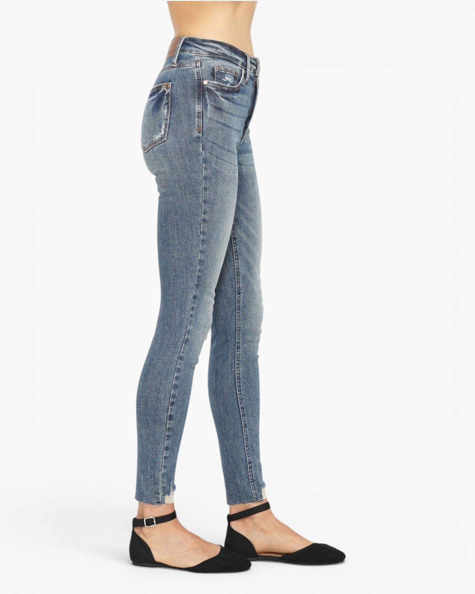 A side profile view of a model wearing light-wash blue skinny jeans and black flat shoes against a plain white background.