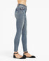 A side profile view of a model wearing light-wash blue skinny jeans and black flat shoes against a plain white background.