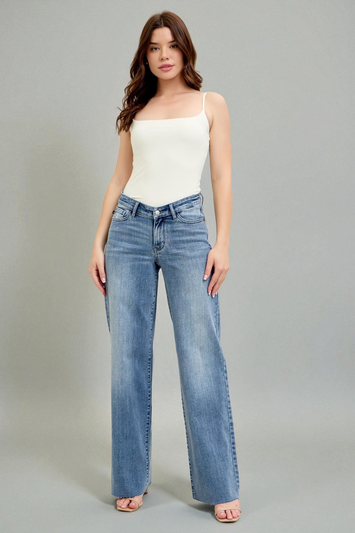 Woman wearing a white top and blue jeans on a gray background