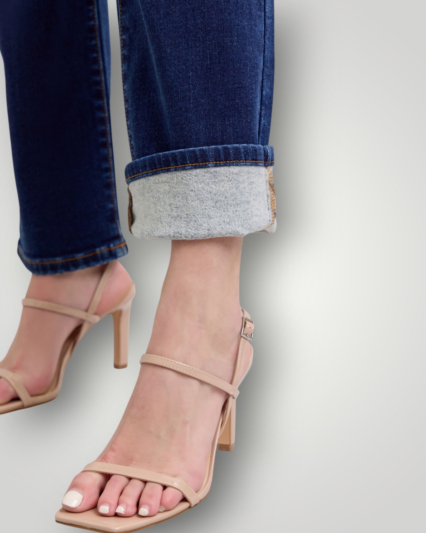 Beige high-heeled sandals worn with rolled-up jeans on a light gray background
