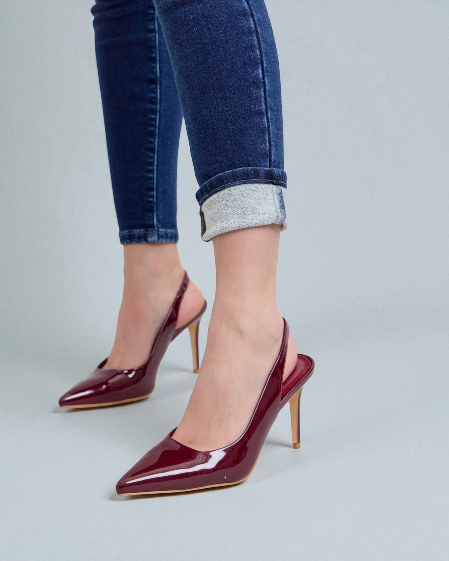 Burgundy high-heeled shoes worn with blue jeans on a light gray background
