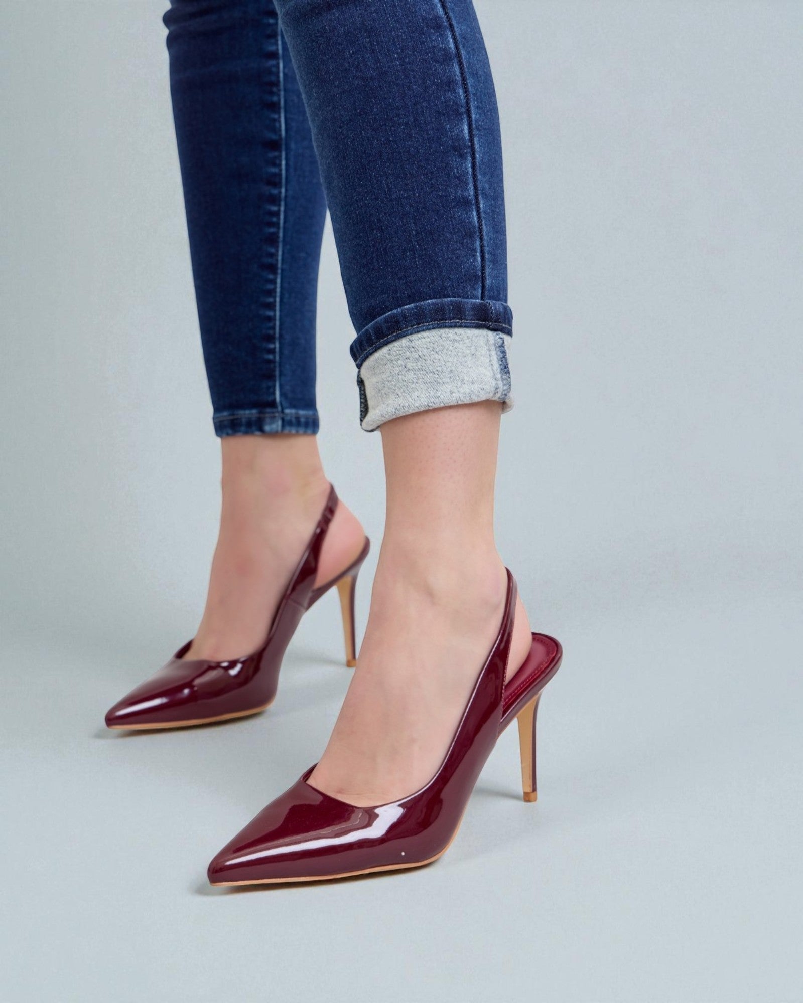 Burgundy high-heeled shoes worn with blue jeans on a light gray background