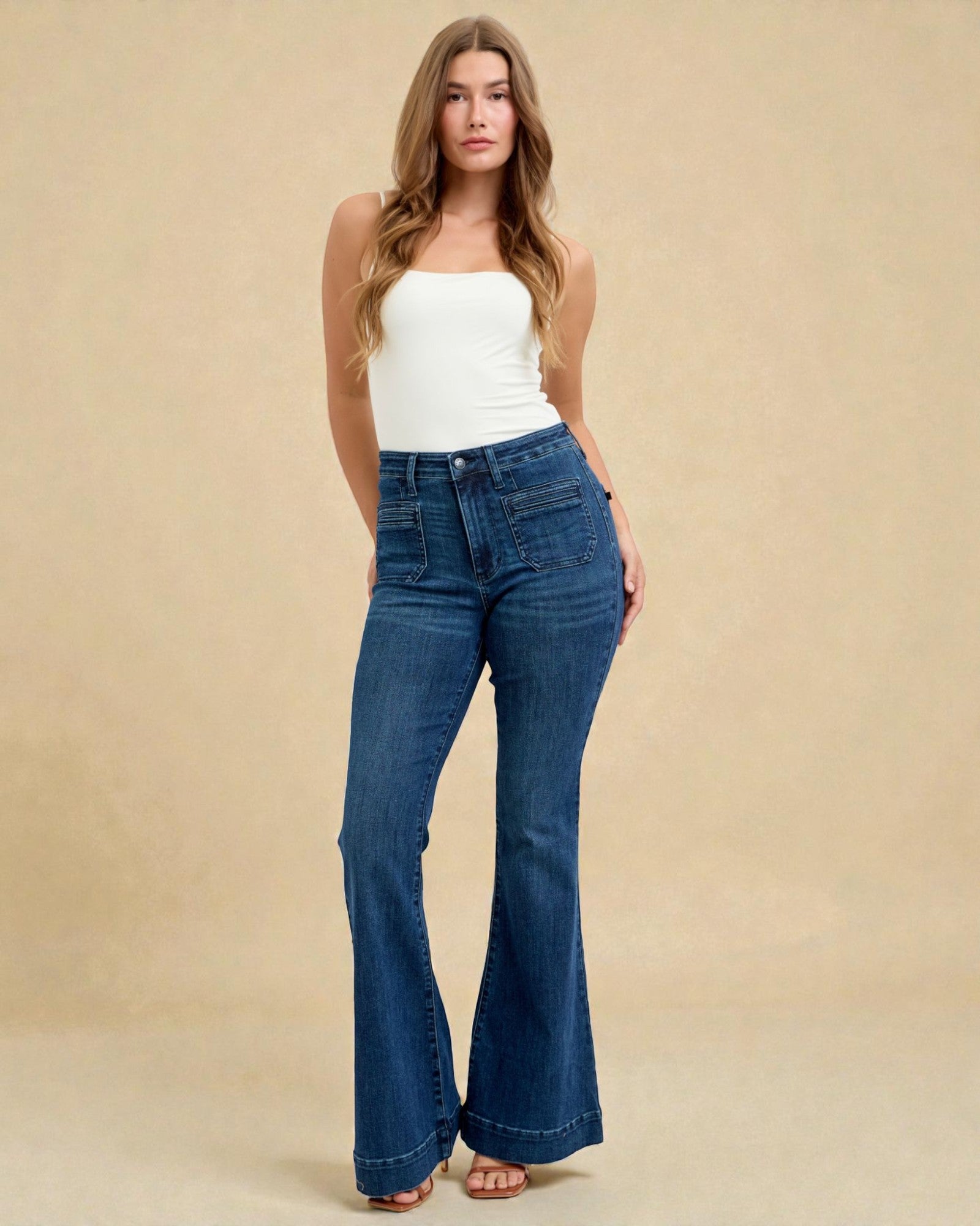 Woman wearing blue flared jeans and a white top on a beige background