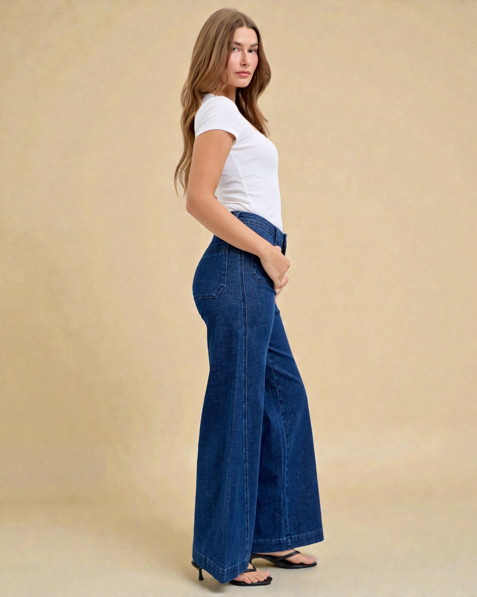 Woman wearing blue wide-leg jeans and a white top on a beige background