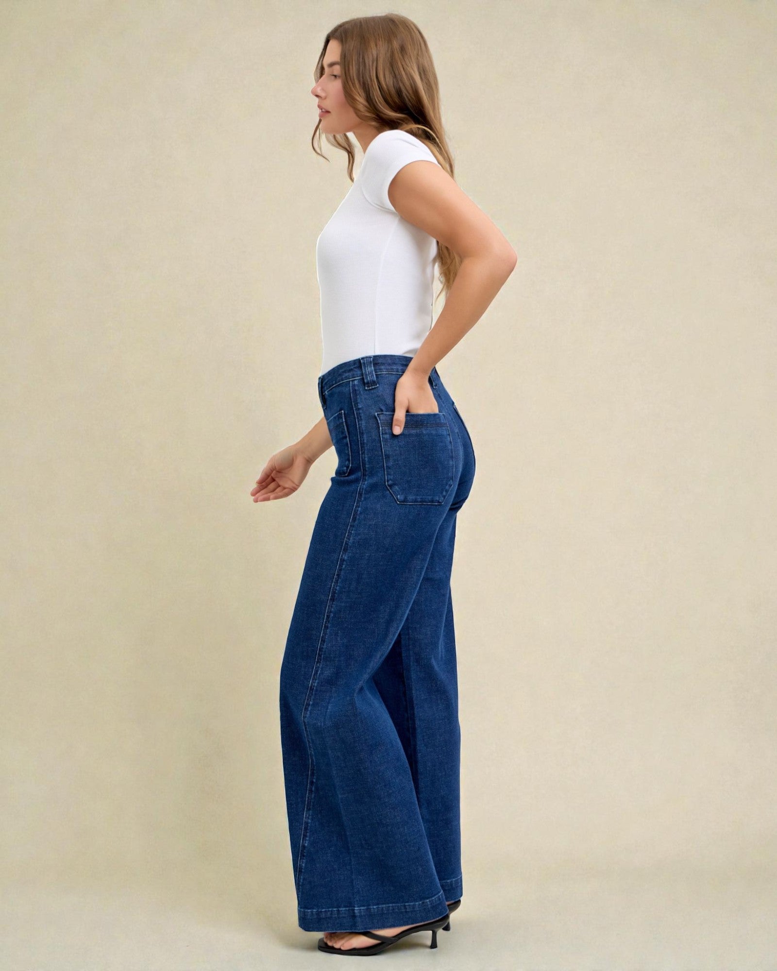 Woman wearing blue wide-leg jeans and a white top on a beige background
