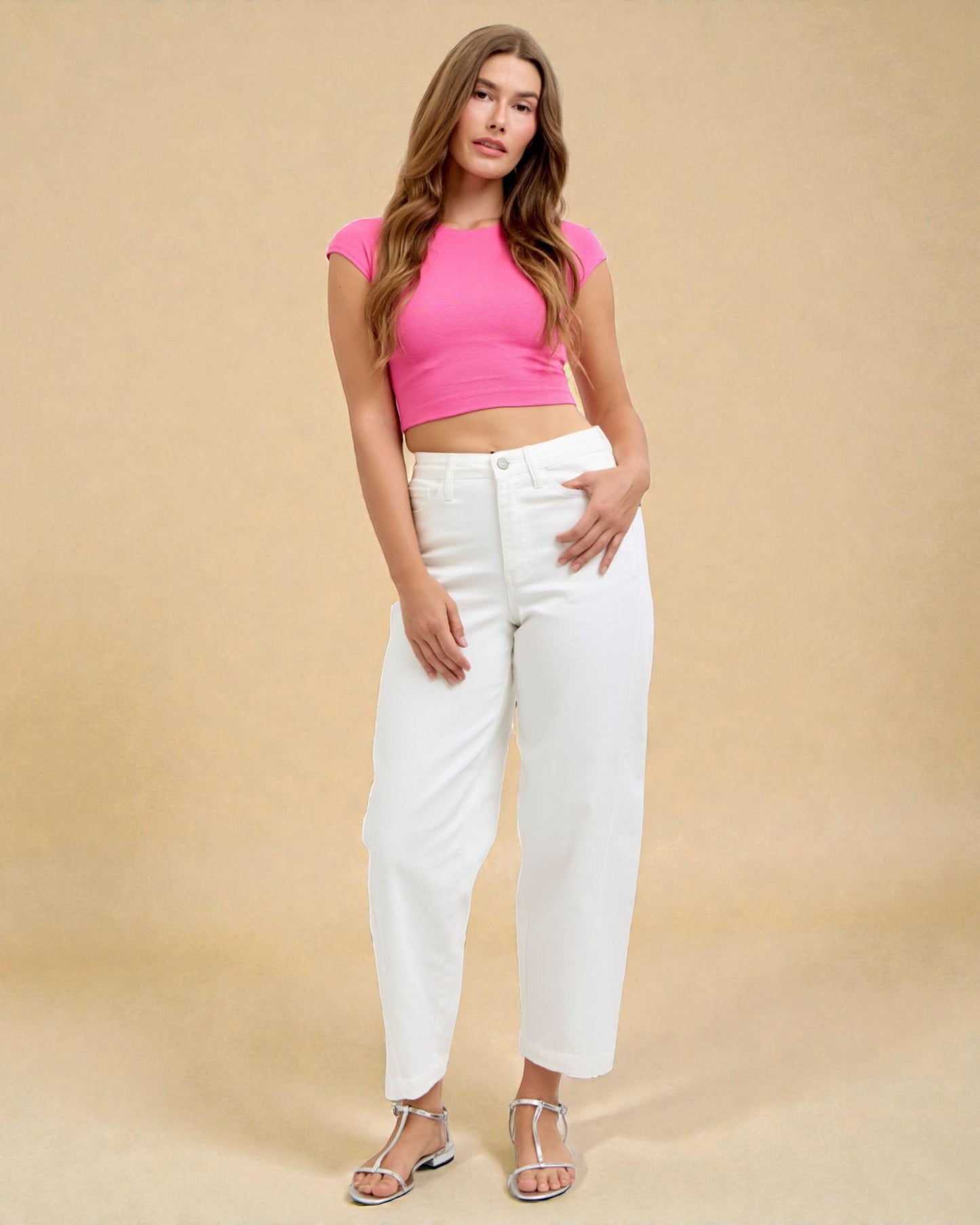 Woman wearing a pink crop top and white pants against a beige background