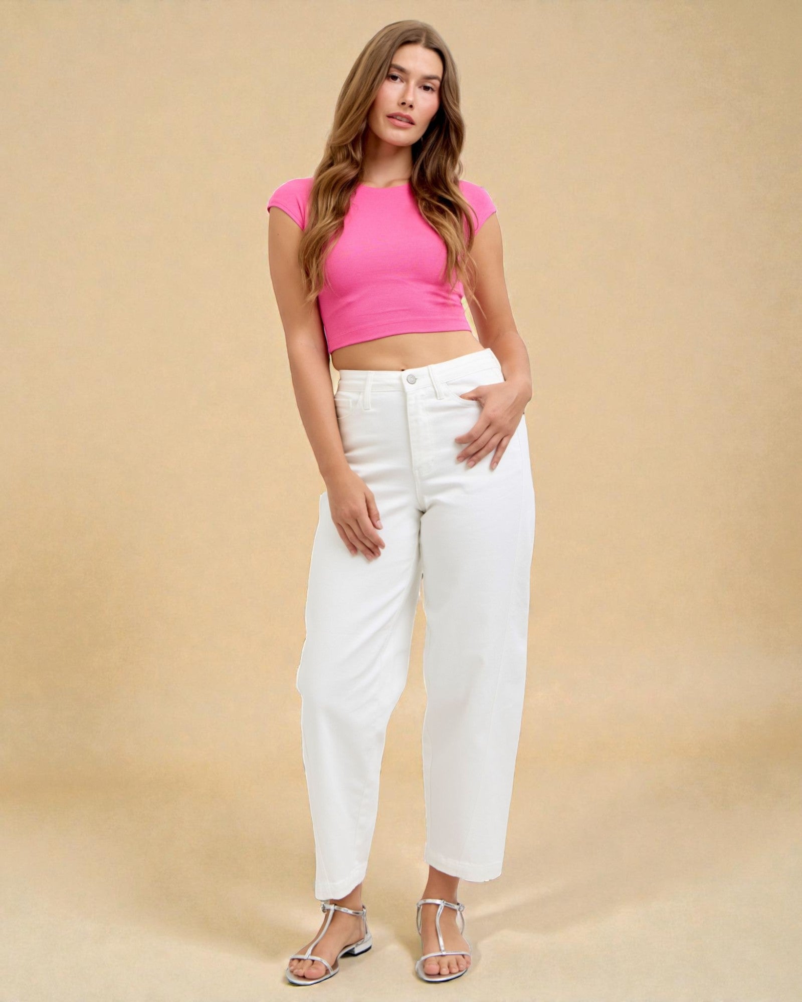 Woman wearing a pink crop top and white pants against a beige background