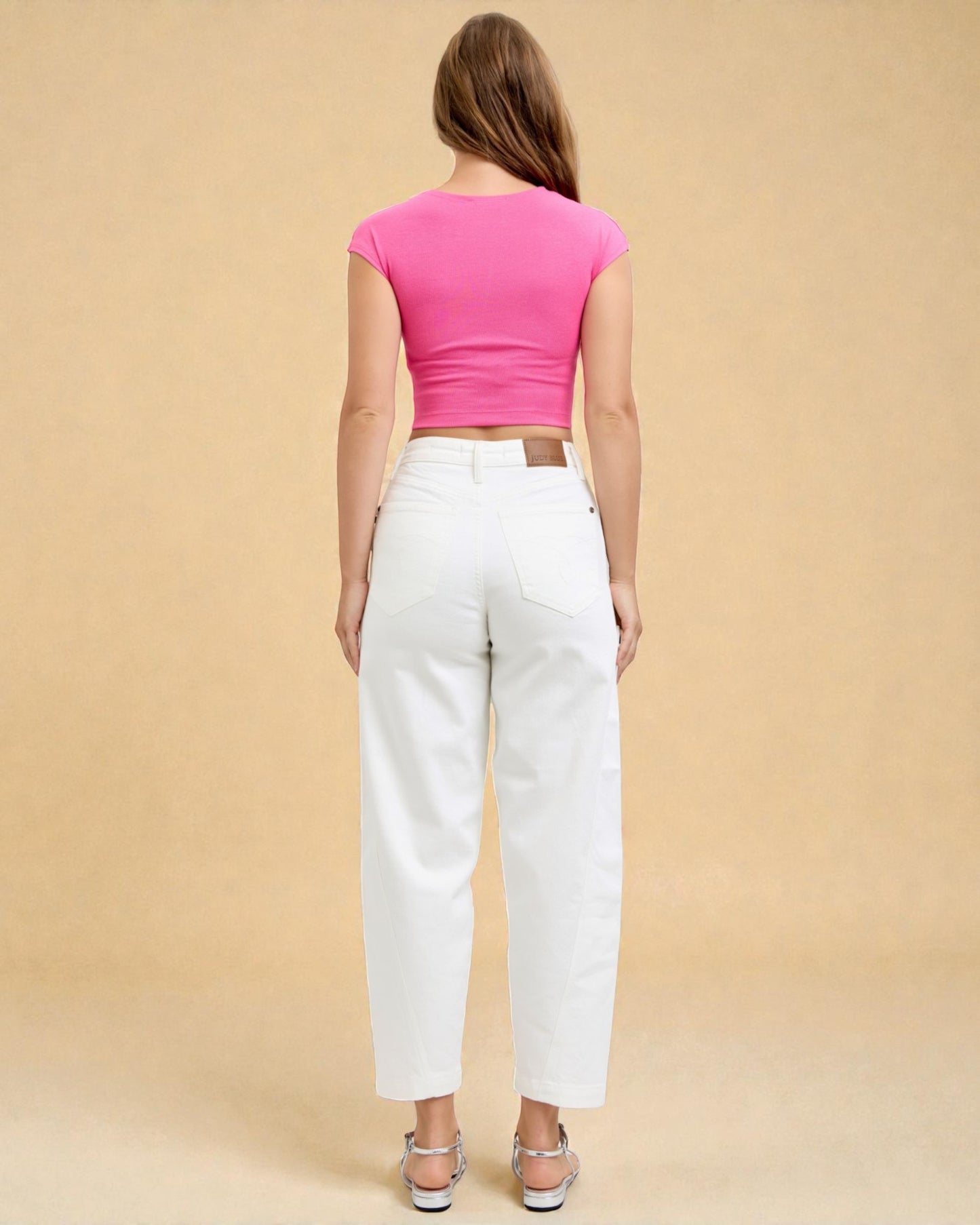 Woman wearing a pink crop top and white pants on a beige background