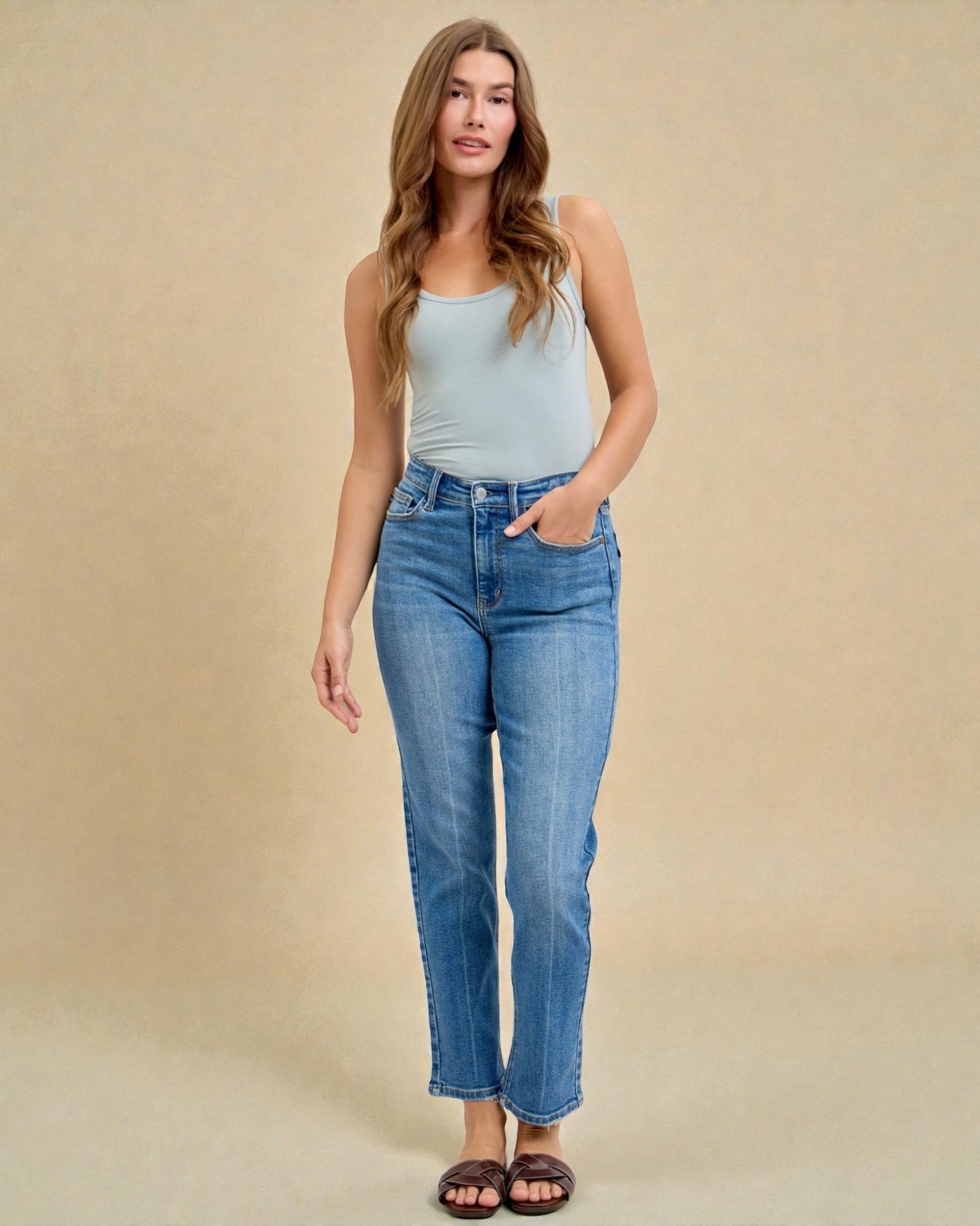 Woman wearing a light blue tank top and jeans against a beige background