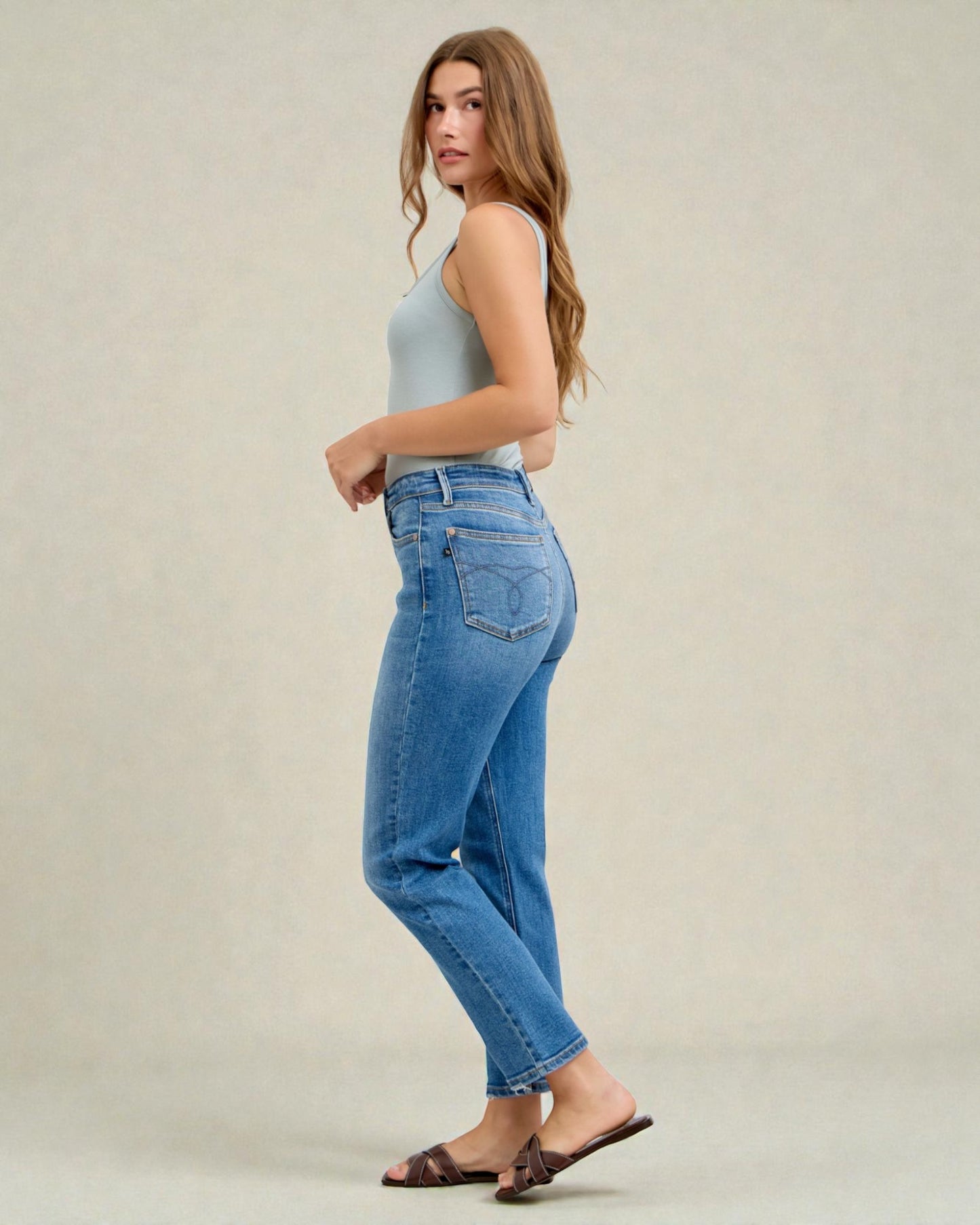 Woman wearing blue jeans and a light gray top on a plain background