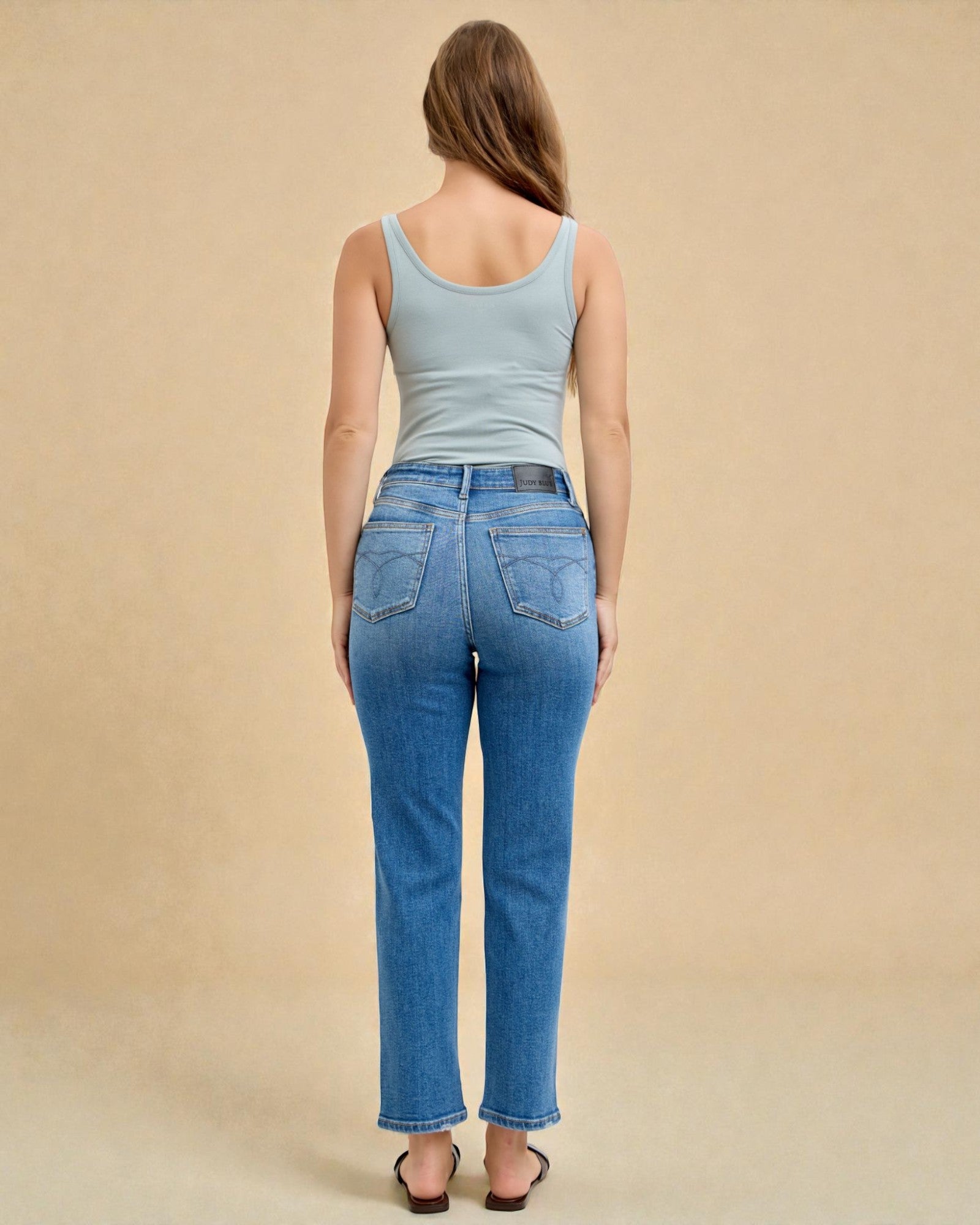 Woman wearing blue jeans and a light blue tank top against a beige background