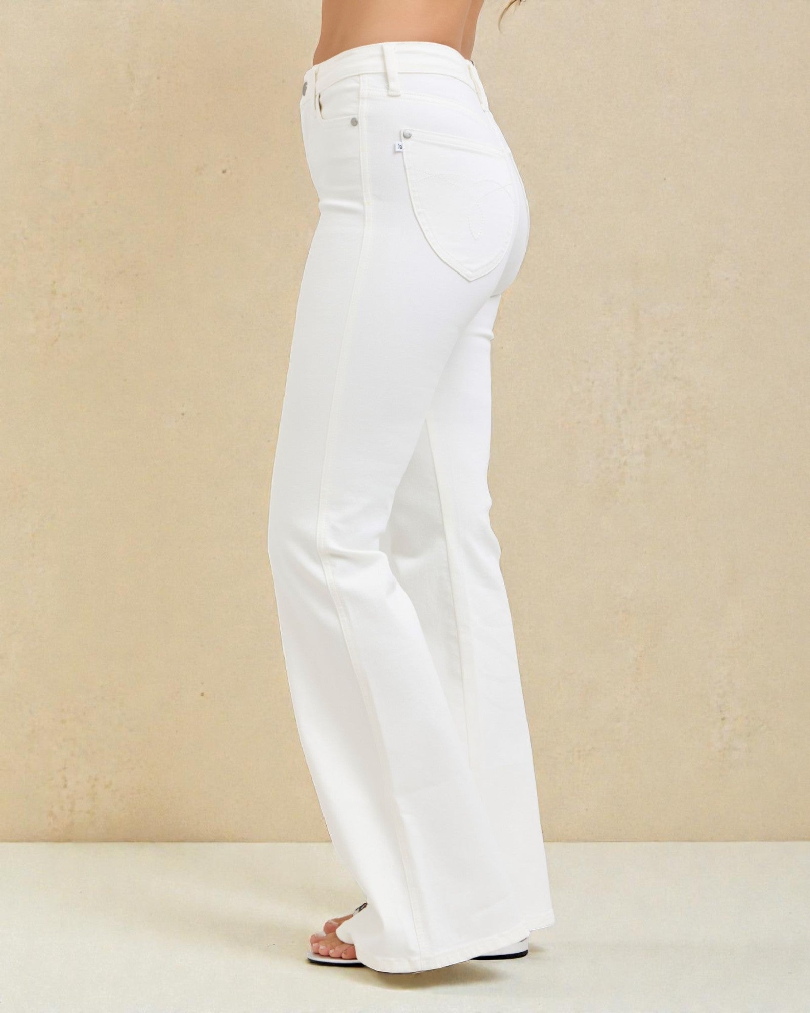 White jeans being worn against a beige background
