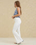 Woman wearing a blue top and white pants against a beige background