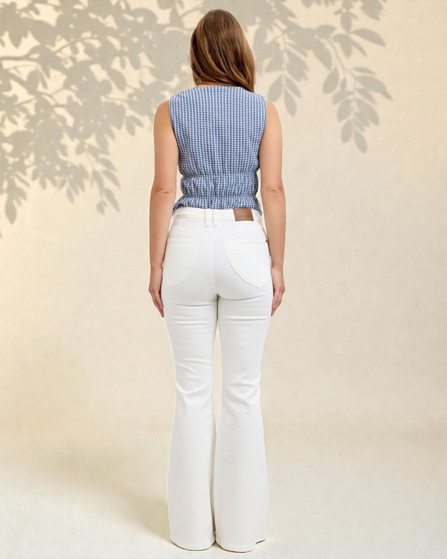 Woman wearing a blue checkered top and white flared pants against a neutral background