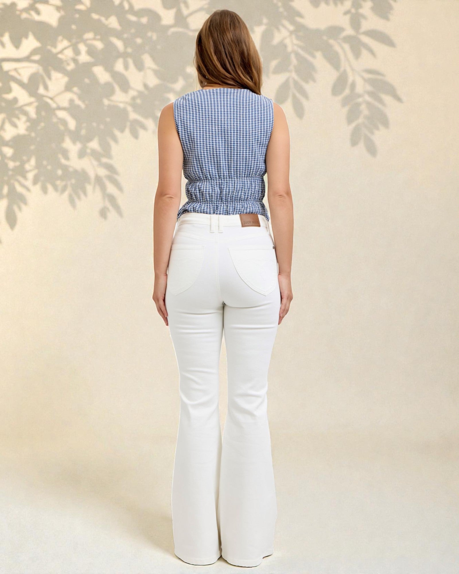 Woman wearing a blue checkered top and white flared pants against a neutral background