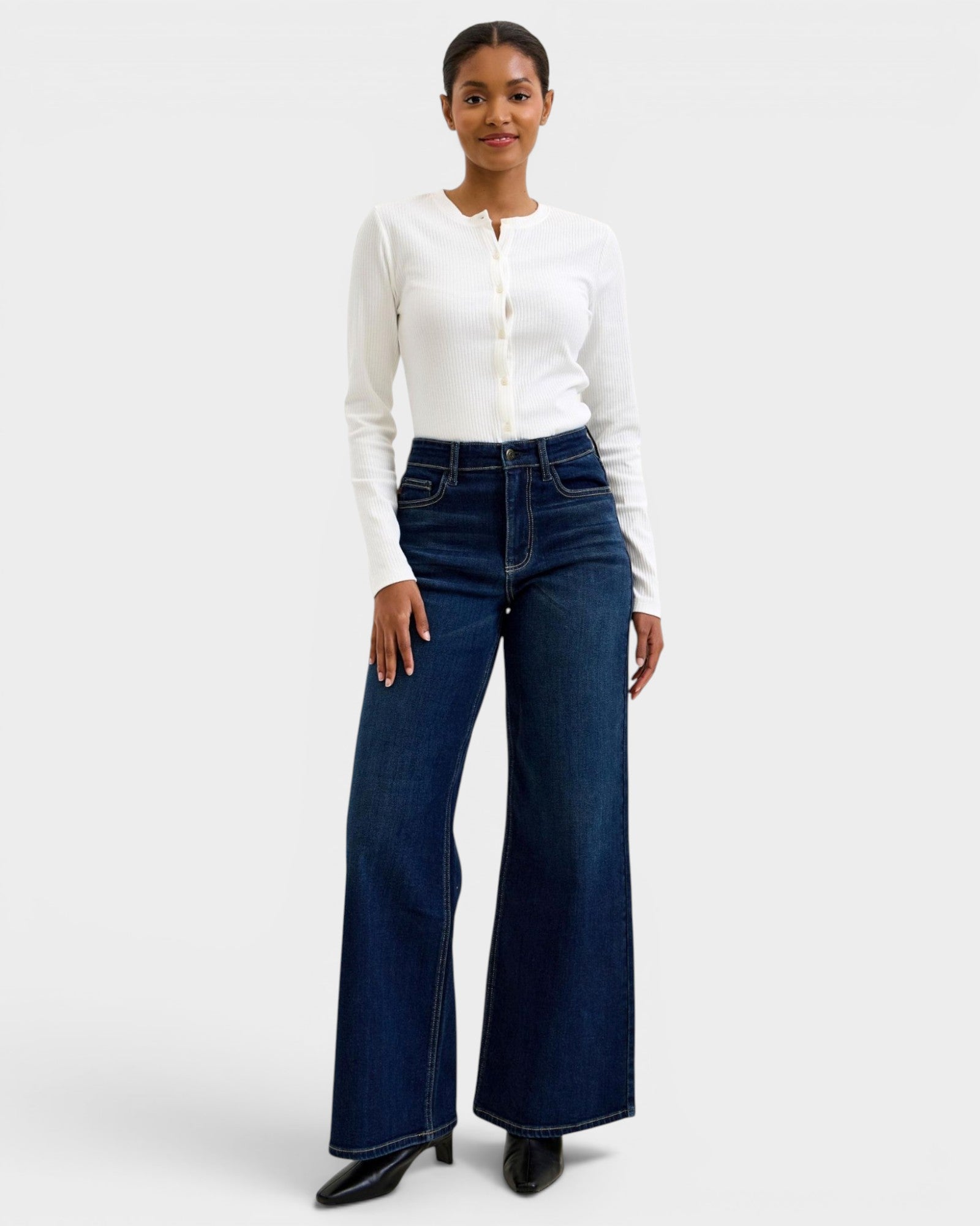 Woman wearing a white long-sleeve top and dark blue flared jeans on a white background