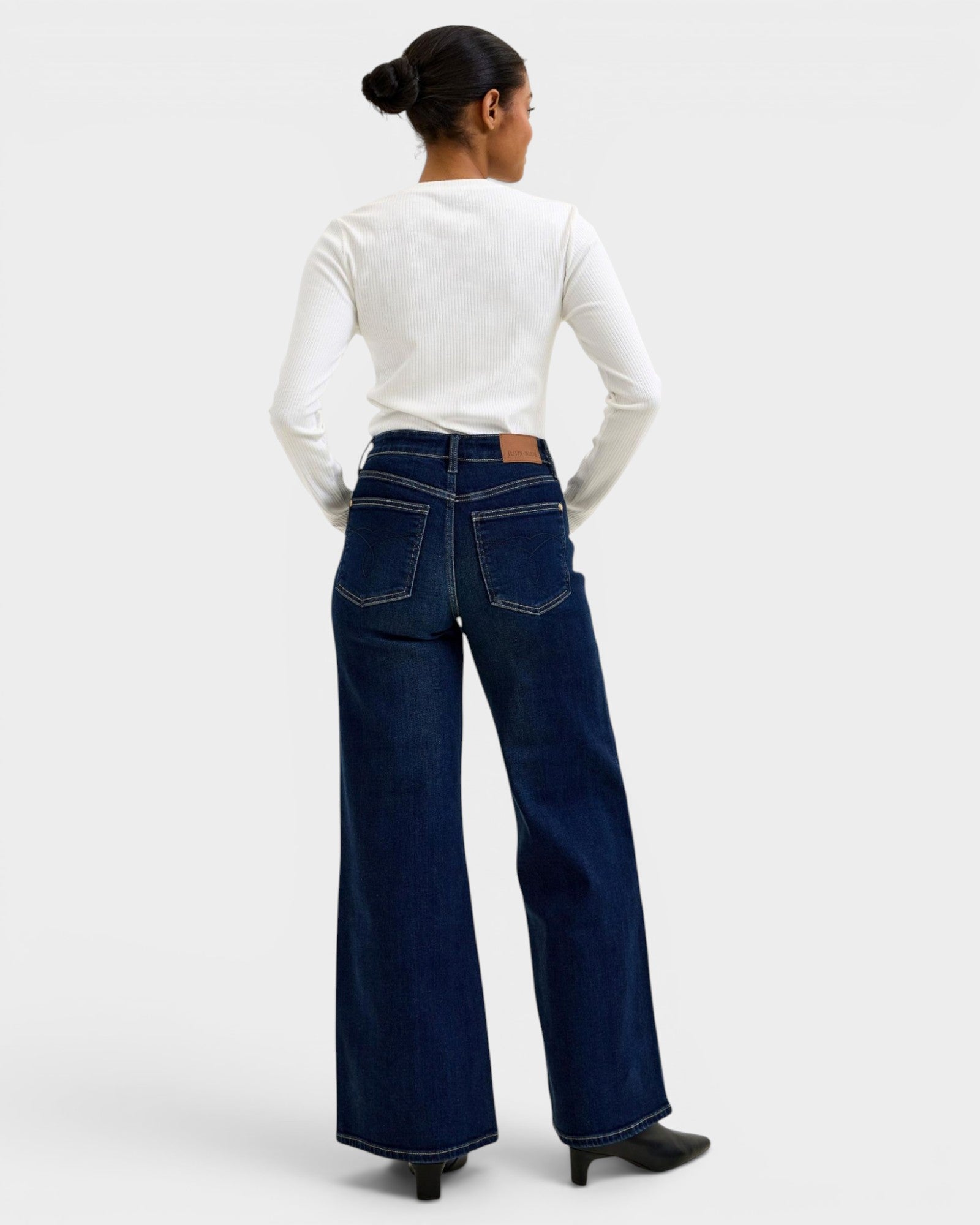 Person wearing dark blue wide-leg jeans and a white long-sleeve shirt on a light gray background